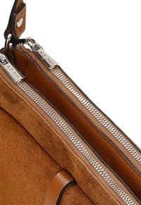Borsa in suede marrone con doppie zip argentate, dettagli in pelle e una texture morbida, che mostra un design compatto con due scomparti principali.