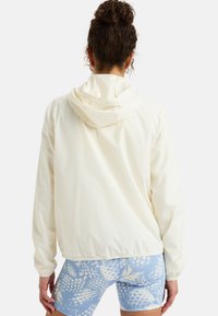 White lightweight jacket with a hood, featuring elastic cuffs and hem. The back shows a smooth texture and relaxed fit.