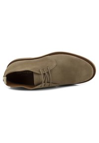 Scarpa chukka in suede marrone con punta rotonda, design con lacci e suola di un marrone chiaro a contrasto, caratterizzata da uno stile minimalista e linee pulite.