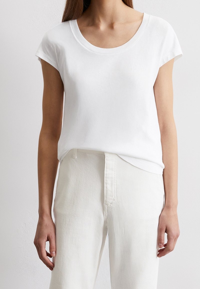 Vit kortärmad T-shirt i mjukt tyg med rundad halsringning, kombinerad med ljusa byxor. Enkelt design, utan mönster eller detaljer.