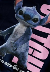 Zils plīša tēls ar lielām acīm un izteiksmīgām ausīm, attēlots tumšā fonā ar rozā teksta elementiem un baltām akcentiem.