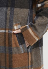Plaid wool coat featuring brown, gray, and white colors, with a side pocket. The fabric has a soft, textured appearance.