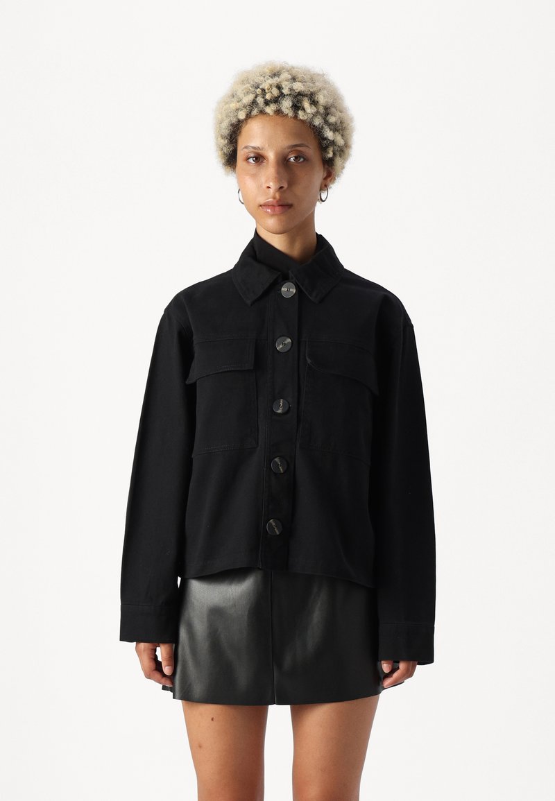 Black jacket with a collar, front button closure, two chest pockets, and long sleeves. Paired with a black leather skirt.