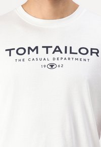 Hvid bomulds T-shirt med fed sort tekst der står "TOM TAILOR THE CASUAL DEPARTMENT 1962." Rund hals, almindelig pasform.