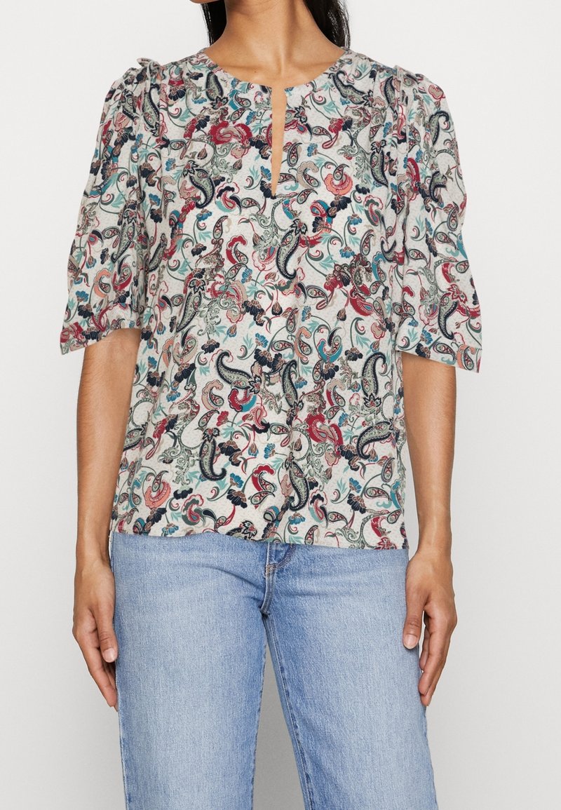 Blusa a fantasia con maniche a palloncino corte, scollatura a chiave e vortici floreali in rosso, blu e verde su uno sfondo chiaro.