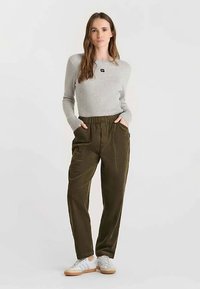 Grijze geribbelde trui met een klein zwart logo, gecombineerd met olijfgroene corduroy broek met zijzakken en witte sneakers.