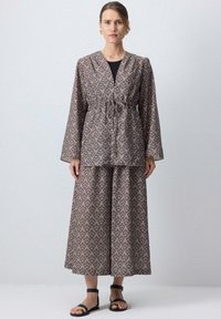 Dvojdielny outfit pozostávajúci z patterned topu s dlhými rukávmi a šnúrkou na sťahovanie a zodpovedajúcej sukne. Farby: tlmená taupe a smotanová. Materiál: mäkká tkanina.