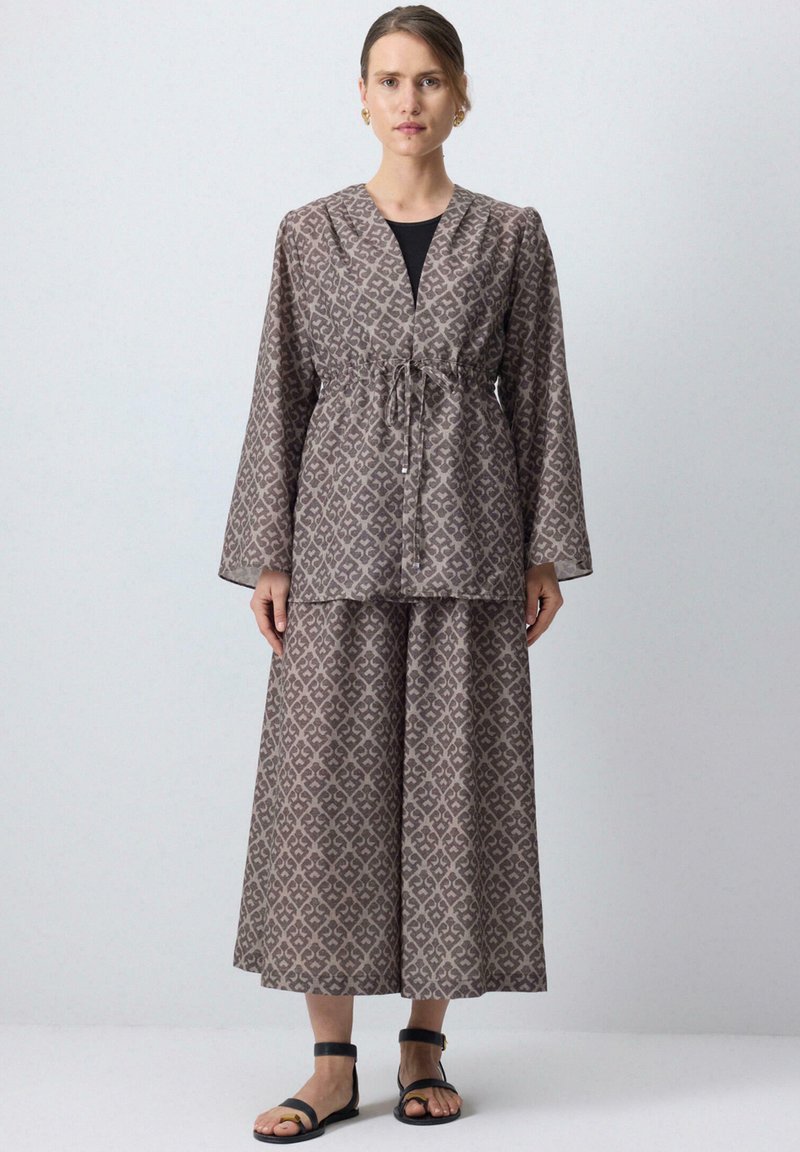 Dvojdielny outfit pozostávajúci z patterned topu s dlhými rukávmi a šnúrkou na sťahovanie a zodpovedajúcej sukne. Farby: tlmená taupe a smotanová. Materiál: mäkká tkanina.