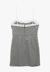 Czarna i biała sukienka mini w kratkę gingham z cienkimi regulowanymi ramiączkami i białą falbaną wokół dekoltu na białym tle.