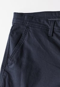 Navy blue fabric pants with a textured finish, featuring a waistline with a belt loop, side pockets, and contrasting stitching detail.