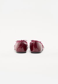 Ballerines en cuir verni bordeaux avec bout rond, présentant un nœud décoratif sur le talon et une semelle plate. Texture lisse.