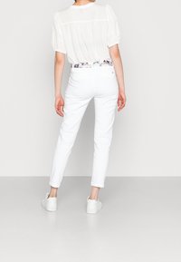 White blouse with puff sleeves, paired with white tapered pants and white sneakers. The belt has a colorful, patterned design.
