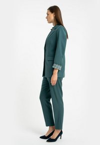 Zestaw w kolorze teal składający się z dopasowanej marynarki z ozdobnymi wzorzystymi mankietami oraz spodni slim-fit, połączony z czarnymi szpilkami.