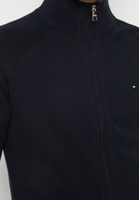 Maglione blu navy con zip realizzato in materiale a maglia testurizzata, con colletto alto e piccolo logo sul petto.