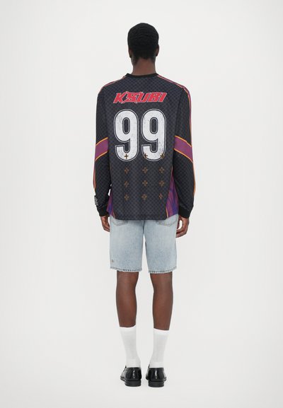 Black long-sleeve jersey with red and purple accents, large white number 99, and cross patterns; paired with light blue denim shorts.
