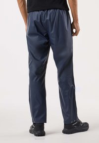 Laivastonsiniset vedenpitävät housut kiiltävästä materiaalista, joissa on joustava vyötärönauha. Suora leikkaus ja säädettävät lahkeensuut. Yhdistetty mustiin kenkiin.