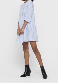 Blauw-wit gestreepte jurk met een uitlopende snit, knoopsluiting en driekwart mouwen, gecombineerd met zwarte haklaarzen.