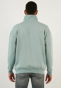 Sudadera de un suave verde menta con un alto cuello, puños y dobladillo acanalados. Fabricada con un material suave y con un diseño de corte holgado.