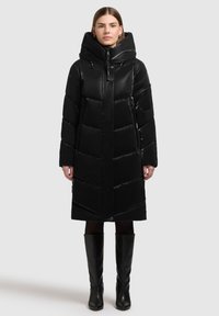 Sort polstret frakke med høj krave og stor hætte. Har en lynlås foran, sidelommer og chevron-quiltet mønster. Sammen med knæhøje støvler.