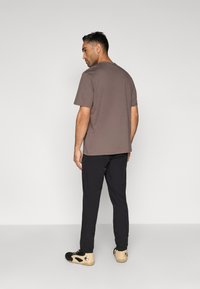 Camiseta castanha de manga curta, de corte solto, combinada com calças pretas e ténis desportivos bege com detalhes pretos. Textura subtil visível no tecido.