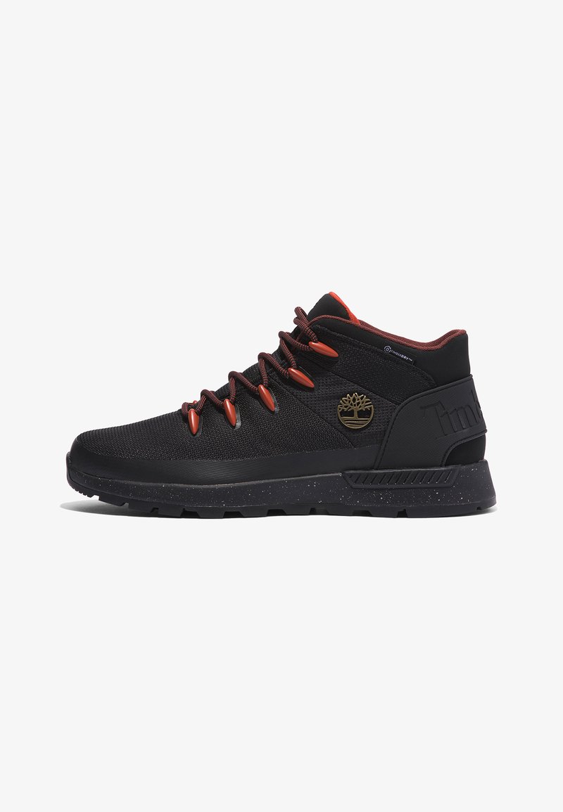 Baskets montantes noires en tissu mesh, avec des lacets rouges et un patch logo. Elles présentent une semelle texturée avec des accents mouchetés.