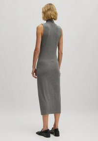 Graues, ärmelloses Rollkragenkleid mit taillierter Silhouette, das bis zur Mitte der Waden reicht. Das Material ist weich und hat eine glatte Textur. Schwarze Schuhe sind sichtbar.