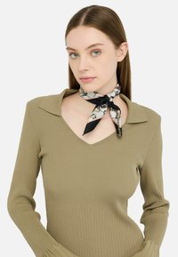 Maglione rigato di colore verde oliva con scollo a V e maniche lunghe, abbinato a una sciarpa di seta fantasia annodata attorno al collo.