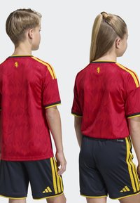 Röd fotbollströja med ett flammtäckt mönster, gula accenter och svarta shorts med gula ränder och logotyp, med fuktavvisande tyg.