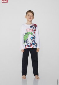 Biała koszula z długim rękawem z grafiką superbohaterów Marvela, w tym Hulka i Spider-Mana, zestawiona z czarnymi spodniami. Gładkie tło.