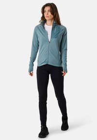 Light blue zip-up jacket with a high collar, textured fabric, and side pockets, paired with black fitted pants and black athletic shoes.