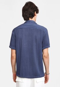 Camisa de manga corta en color azul marino con un patrón texturizado de panal. Cuenta con cuello y un corte relajado; fabricada en material transpirable.