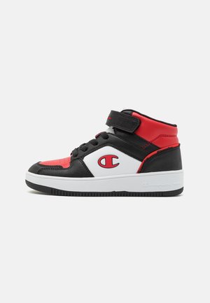 Mid-top sneaker met zwarte, rode en witte panelen, een klittenbandsluiting en een groot rood "C"-logo aan de zijkant en een witte zool.