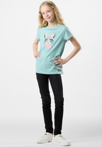 Light blue cotton t-shirt featuring a cat graphic with sunglasses and a pink patterned scarf. Paired with black jeans and white sneakers.