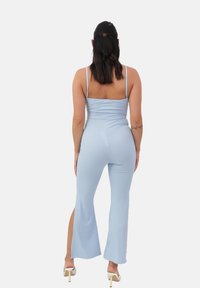 Monos de color azul cielo con canalé, tirantes delgados, corsé ajustado y pantalones acampanados con aberturas laterales, complementados con tacones altos de tonos claros.