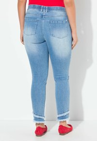 Jeans skinny de mezclilla azul claro con dobladillo deshilachado, que cuentan con una cinturilla elástica y dos bolsillos traseros. Llevados con unos zapatos planos rojos.