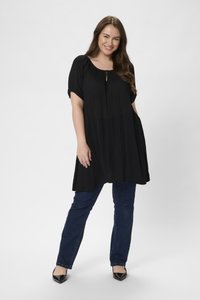 Tunique noire à manches courtes, décolleté en forme de clé, coupe ample, associée à un jean bleu foncé et des ballerines noires à bouts pointus. Design simple.