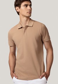 Beżowa koszulka polo z klasycznym kołnierzykiem, krótkimi rękawami i dopasowanym krojem. Posiada jedną zapięcie na guziki i gładką teksturę bawełnianego materiału.