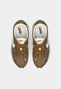 Bruine Nike sneakers featuring ingewikkelde patronen, gestructureerde stof en een wit swoosh-logo. Bruine veters en licht gewatteerde binnenzolen.