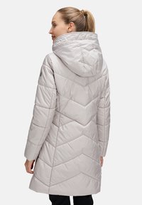 Ljusgrå vadderad jacka med huva, med ett chevronquiltat mönster och långa ärmar. Materialet ser glatt och glänsande ut.