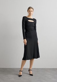 Μαύρο φόρεμα με μακριά μανίκια που διαθέτει κοπή στο μπροστινό μέρος, στενή ζώνη και φουσκωτό στρίφωμα. Λείος ύφασμα με ελάχιστες λεπτομέρειες. Κομψή σιλουέτα.