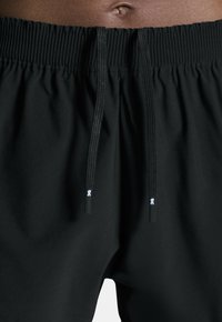 Svarta atletiska shorts med elastisk midja och snoddar. Tyget är slätt och lätt, designat för komfort och rörlighet.