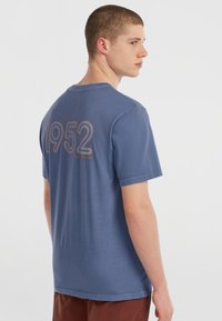 Blå bomulds t-shirt har rund hals og korte ærmer, med "1952" trykt i stort omrids skrift på ryggen.
