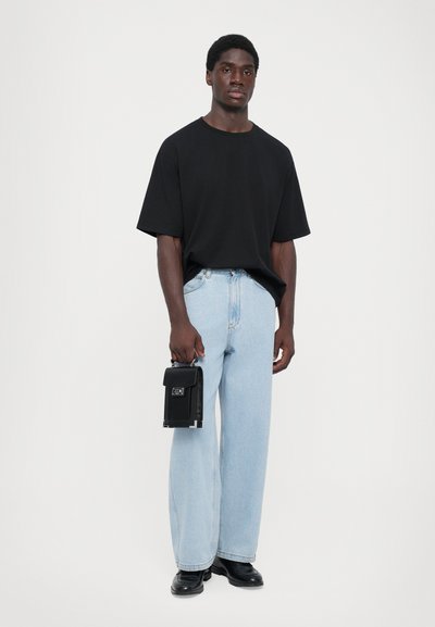 Czarny oversize T-shirt, jasnoniebieskie szerokie spodnie dżinsowe, czarna torba z uchwytami, czarne buty. Prosty, czysty design z różnorodnymi teksturami.
