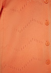 Cardigan in maglia corallo con una texture liscia, caratterizzato da un motivo a onde creato da dettagli intagliati e bottoni coordinati.