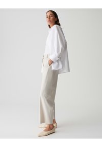 Weißes, übergroßes Hemd mit Knöpfen, beigefarbene, hochgeschnittene Hose und cremefarbene flache Schuhe. Glatte Stoffe, lockere Passform und minimalistisches Design.