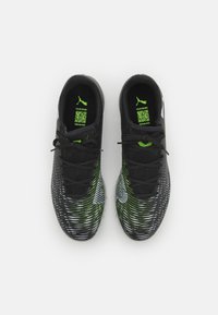Zapatillas deportivas negras con parte superior texturizada, que presentan acentos verdes y un patrón dinámico. Se pueden ver los cordones y un logo en el lateral.