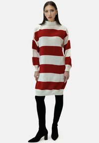 Rood-wit gestreepte gebreide jurk met hoge hals en lange mouwen, gecombineerd met zwarte leggings en enkellaarsjes met een puntige neus.