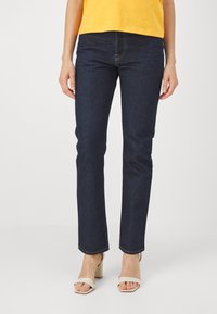 Jeans in denim blu scuro con un design a gamba dritta, cuciture in evidenza e vita media, abbinati a scarpe con tacco a blocco beige.