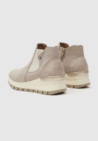 Un par de botas de tobillo de ante beige con paneles elásticos en los laterales, cremallera trasera, suelas de plataforma gruesa color crema y suelas con textura sobre un fondo claro.