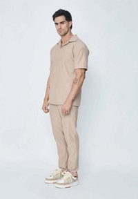 Polo shirt beige à manches courtes, texturé, et pantalon slim assorti. Porté avec des baskets multicolores. Design simple, détails minimaux.